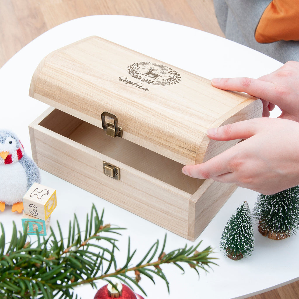 Wooden jewelry box with a hand opening it, surrounded by Christmas decorations.