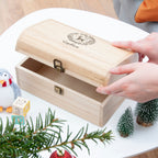 Wooden jewelry box with a hand opening it, surrounded by Christmas decorations.