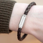 Brown braided bracelet with a silver tag on a wrist, brand 'FRASER' visible