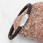 Brown braided leather bracelet with silver clasp on a textured stone surface
