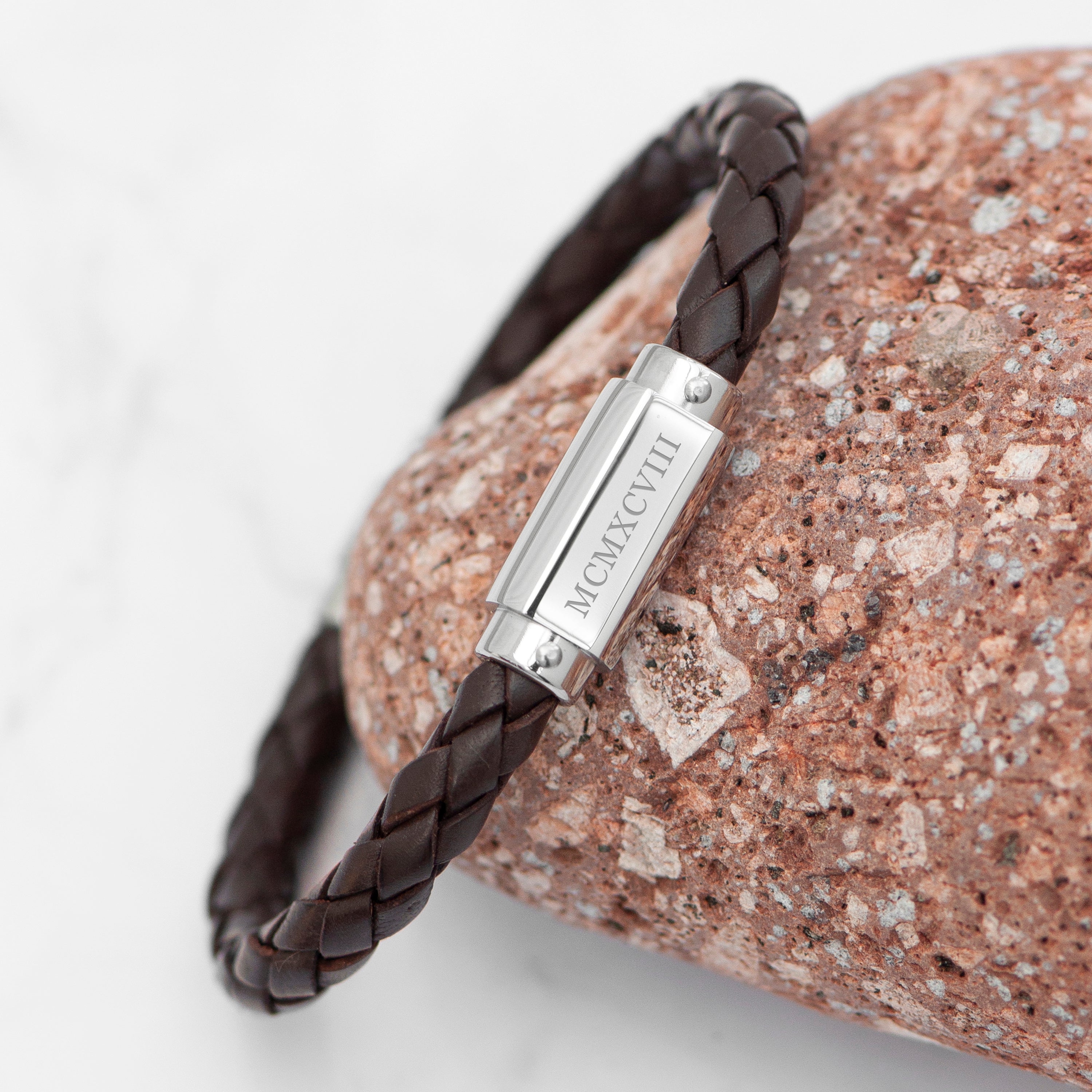 Brown braided leather bracelet with silver clasp on a textured stone surface