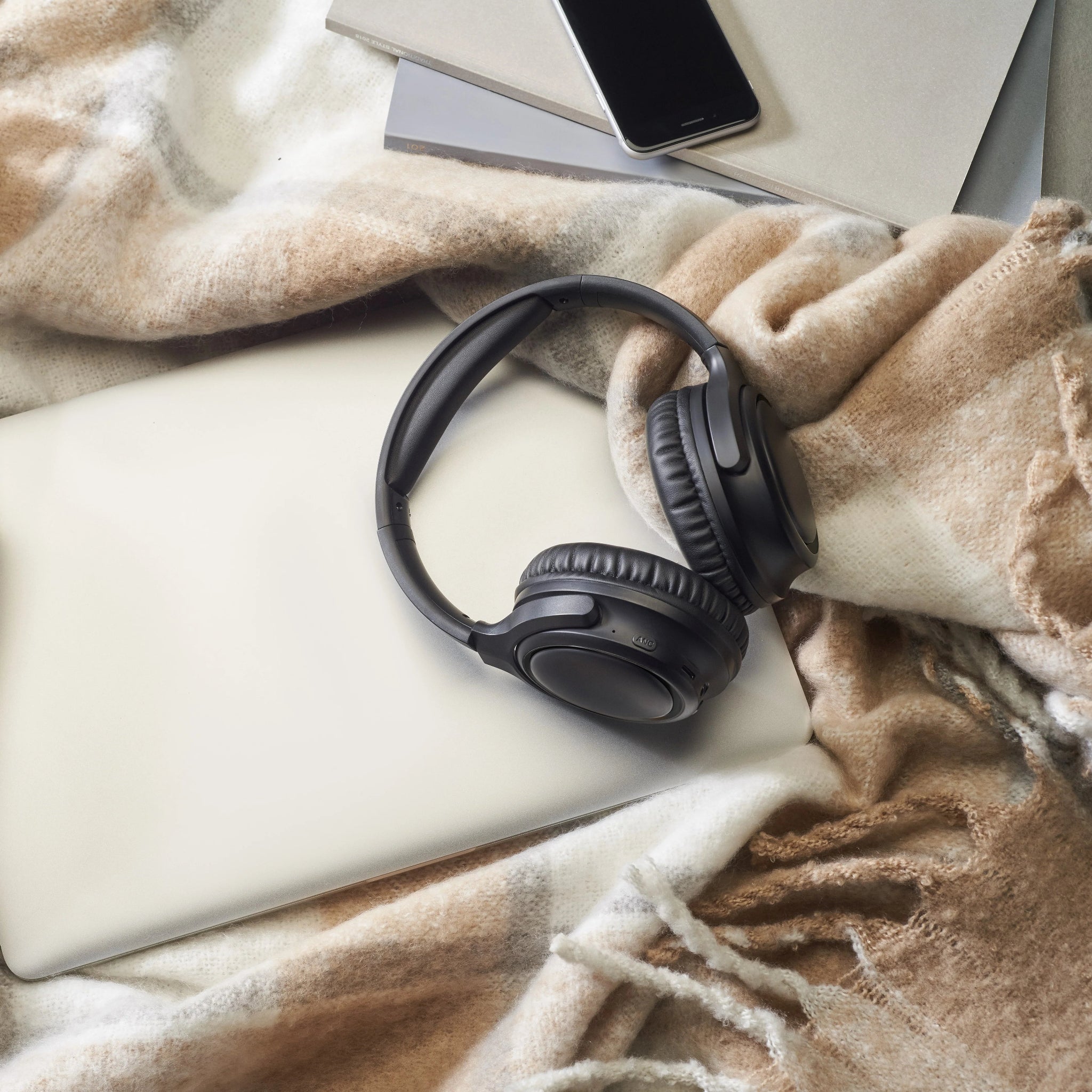 Black headphones on a white surface with a beige blanket