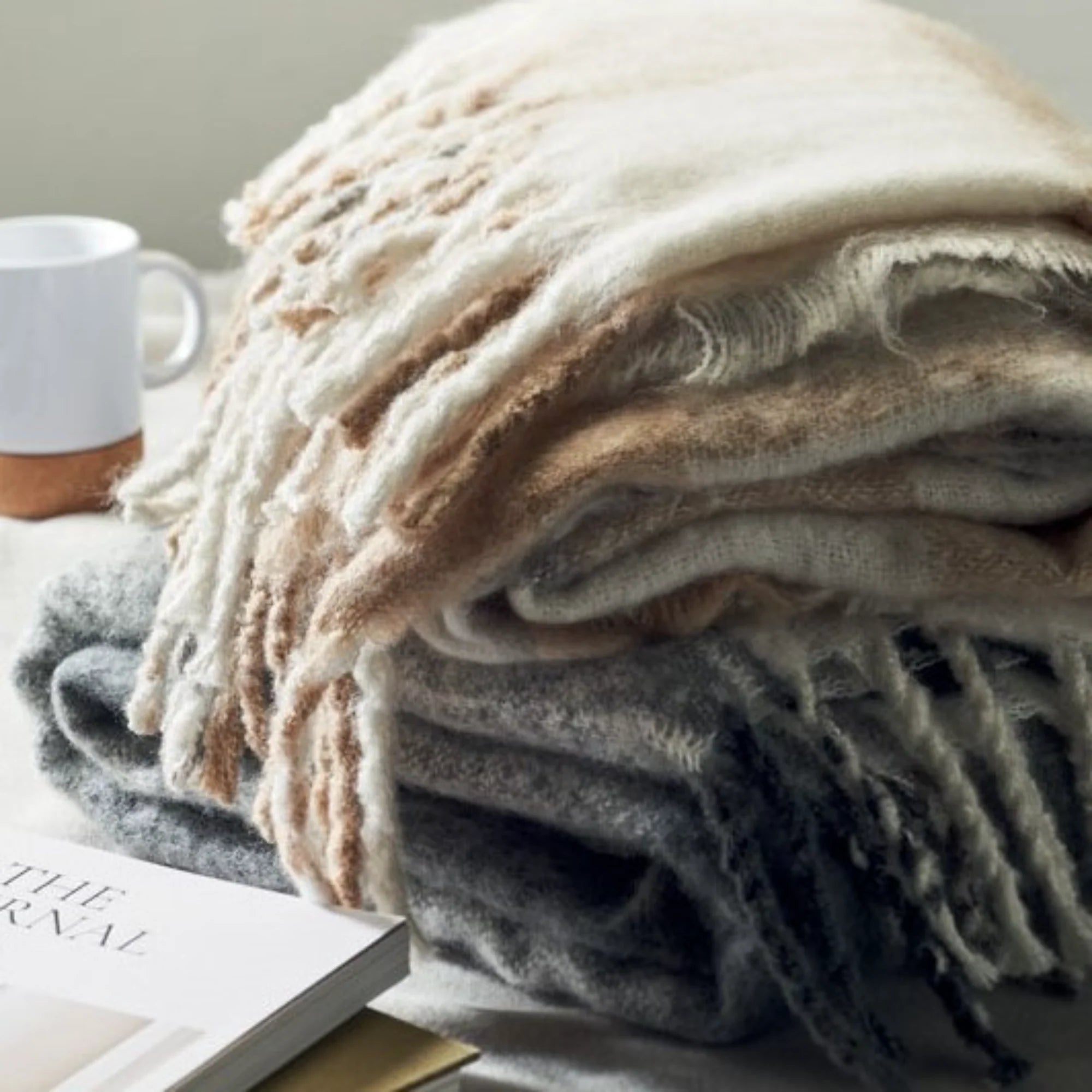 Stack of folded blankets with a mug and book in the background