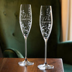 Two personalized champagne flutes with engraved names on a wooden surface.