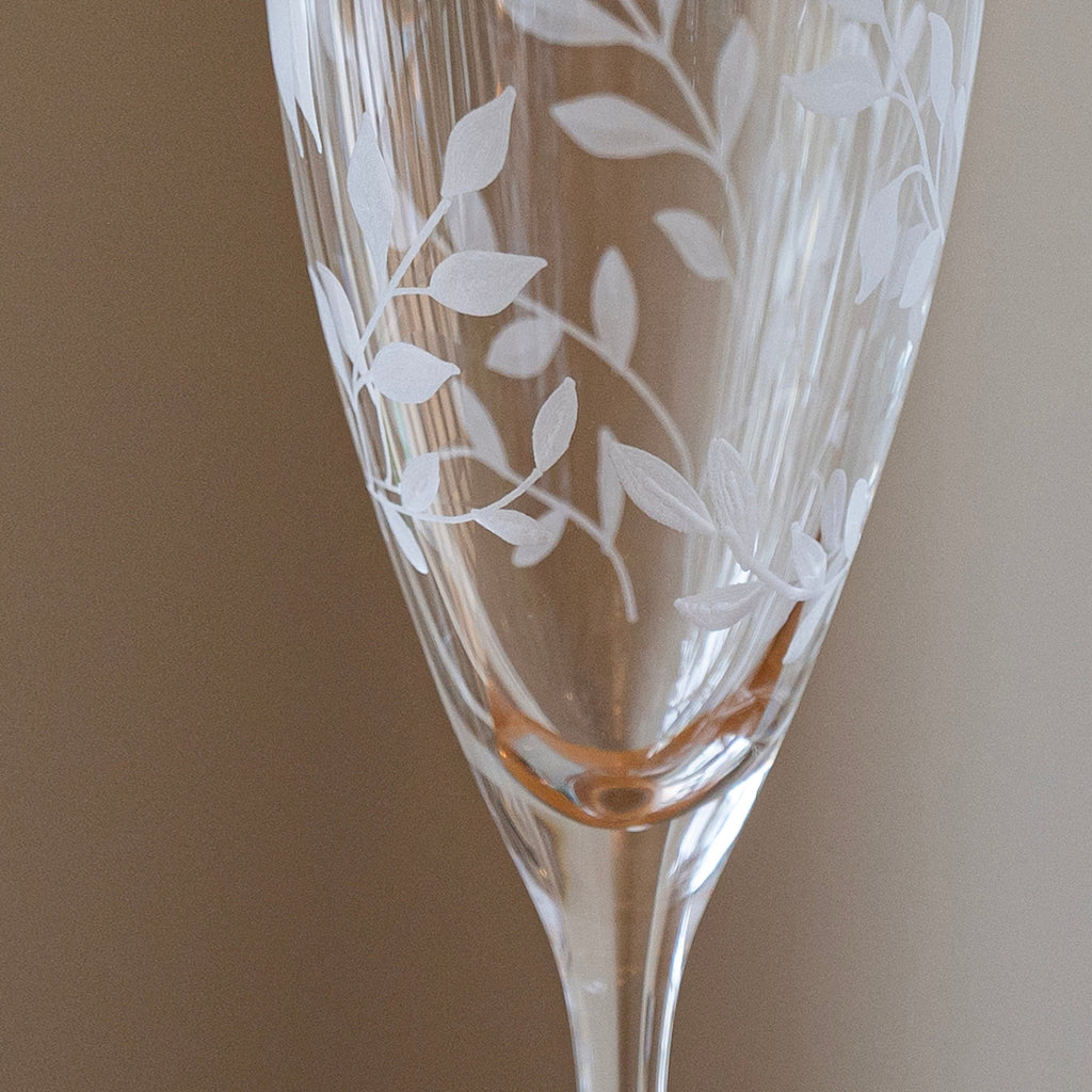 Etched glass flute with leaf patterns on a plain background
