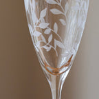 Etched glass flute with leaf patterns on a plain background
