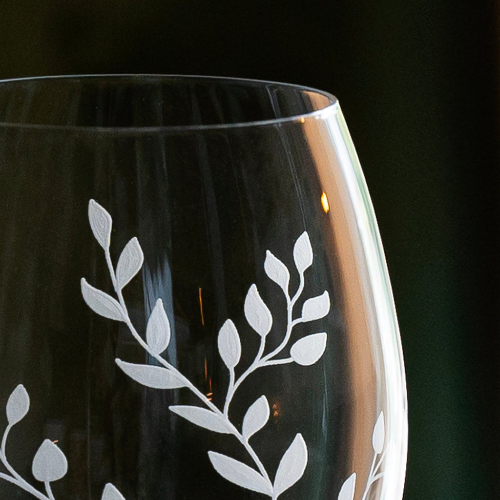 Black wine glass with white leaf etching on a dark background