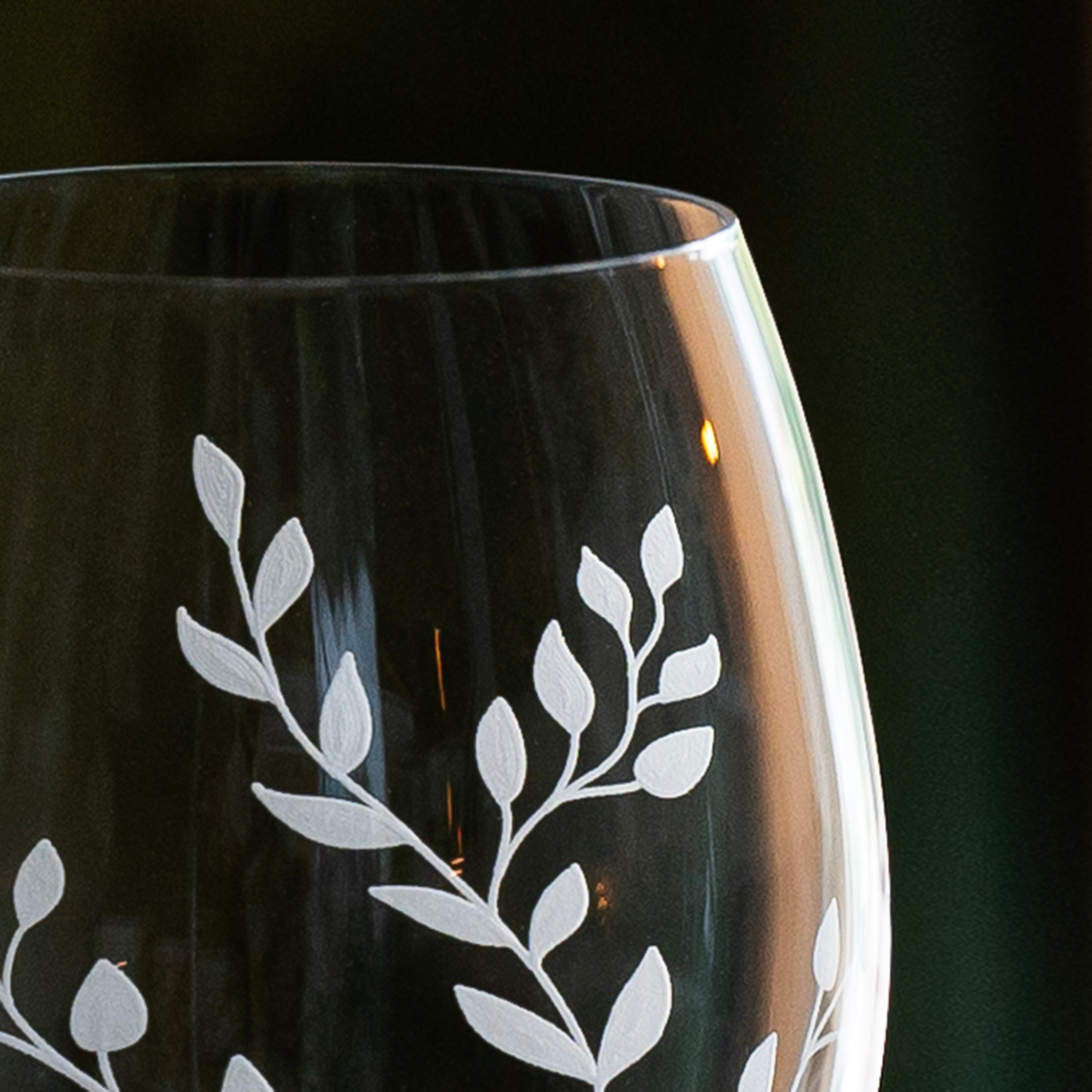 Black wine glass with white leaf etching on a dark background