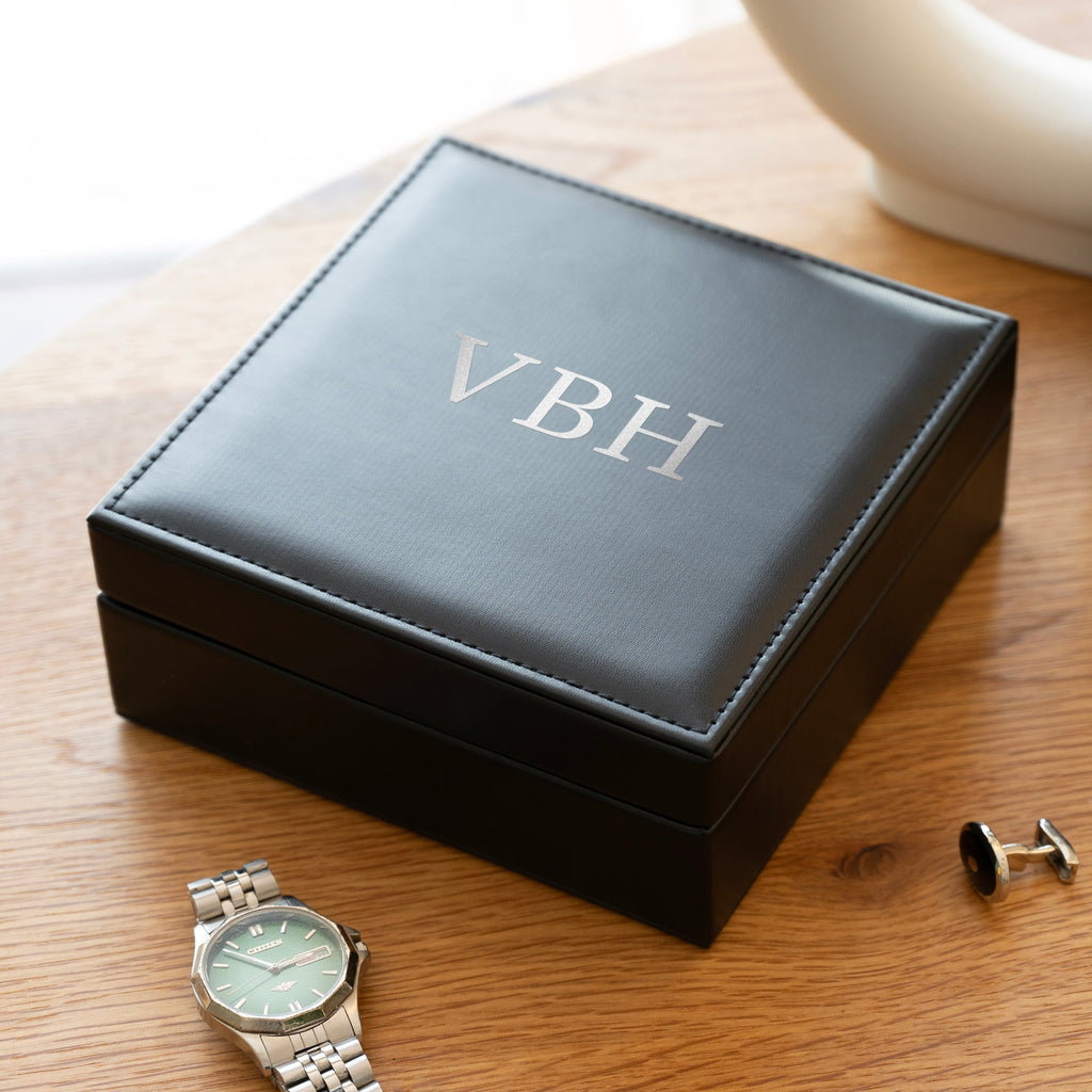 Black jewelry box with 'VBH' initials, a watch, and cufflinks on a wooden surface.