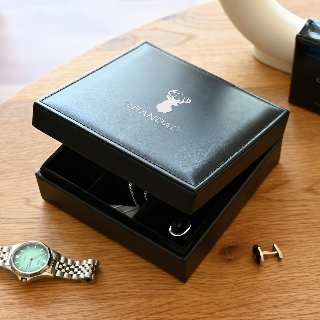 Open black jewelry box with 'RB' initials on a wooden surface, containing a watch and cufflinks.
