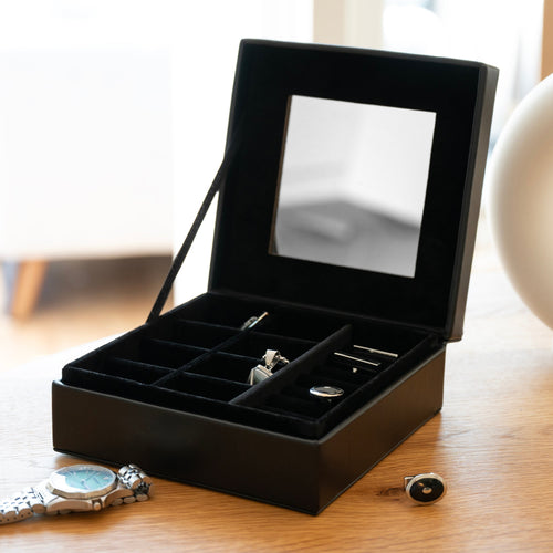 Black jewelry box with mirror lid containing cufflinks on a wooden surface.