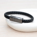 Black braided leather bracelet with engraved silver tag on a white stone surface