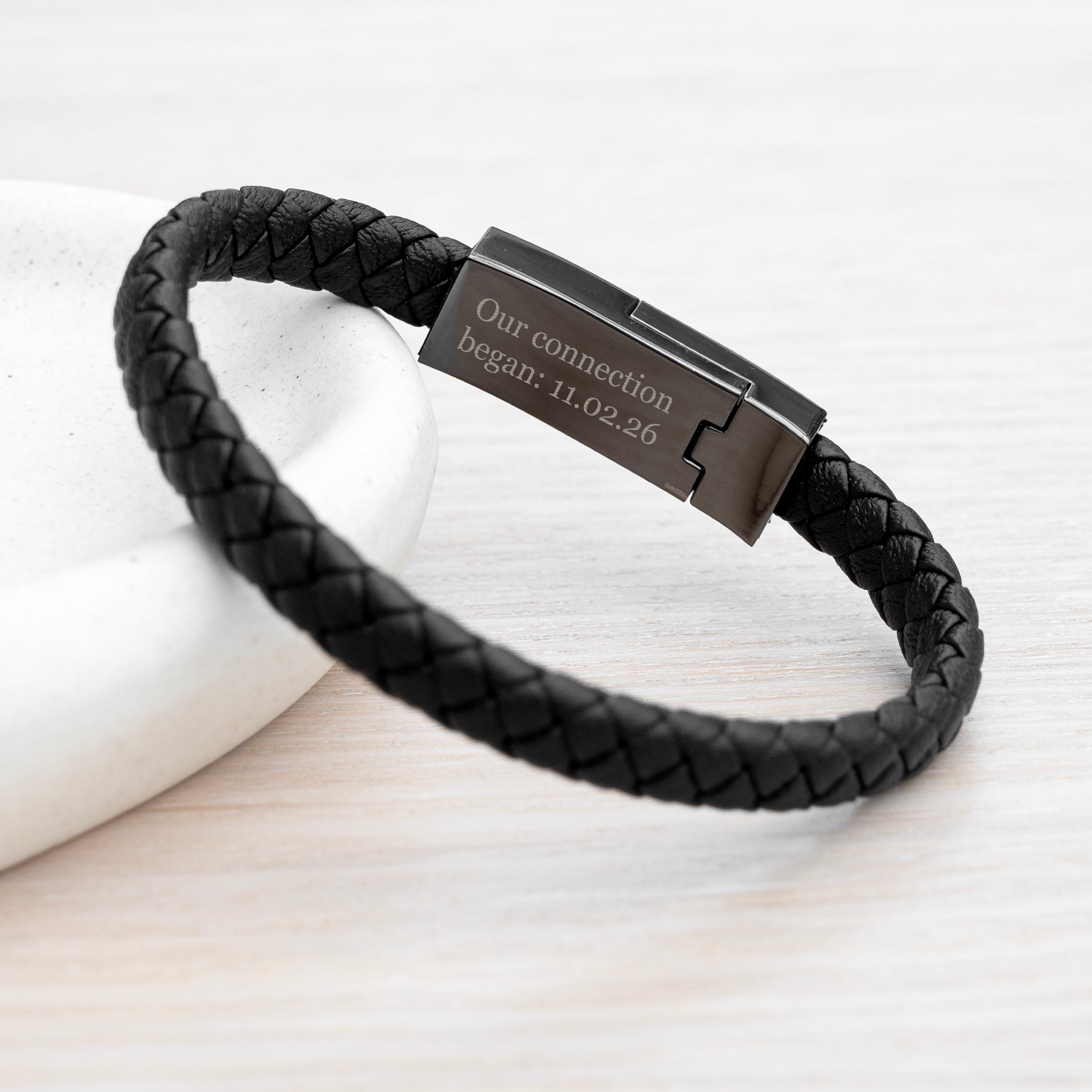 Black braided leather bracelet with a metallic tag on a light background