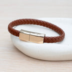 Brown braided leather bracelet with a gold clasp on a light background
