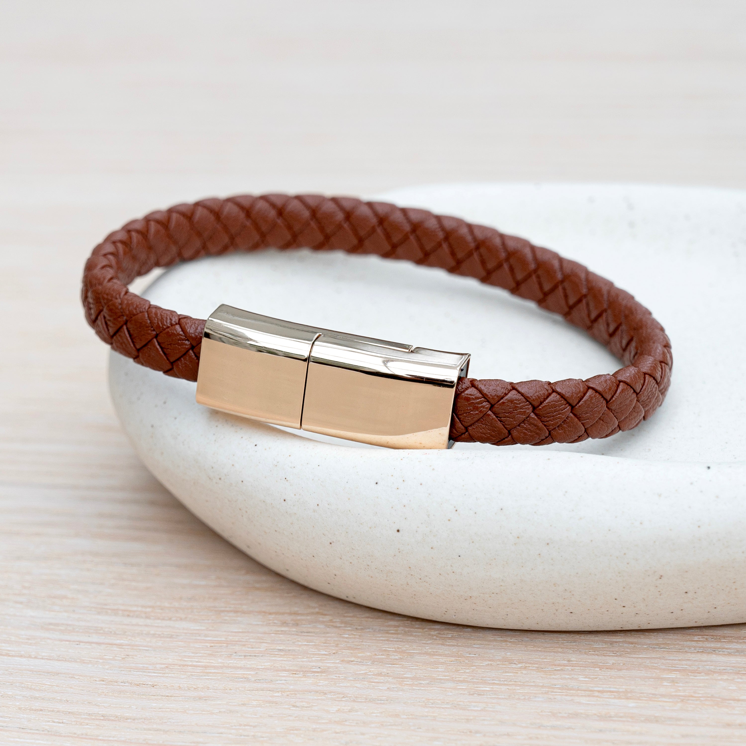 Brown braided leather bracelet with a gold clasp on a light background