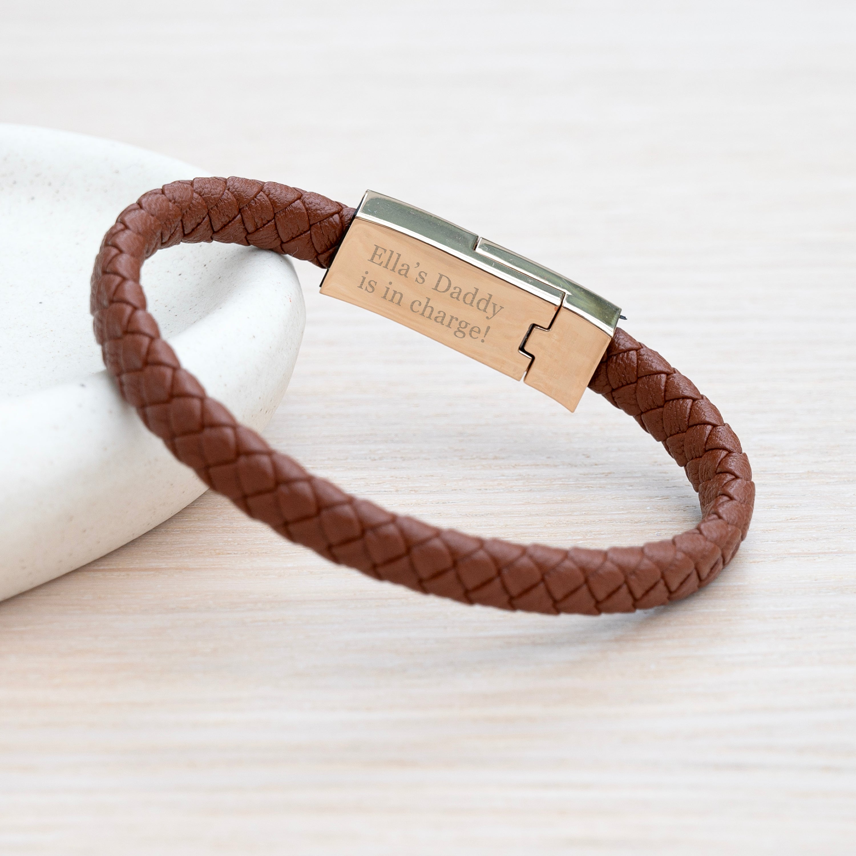 Brown braided leather bracelet with a metal tag on a light background