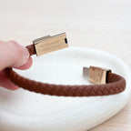 Brown braided leather bracelet with gold clasp on a white surface