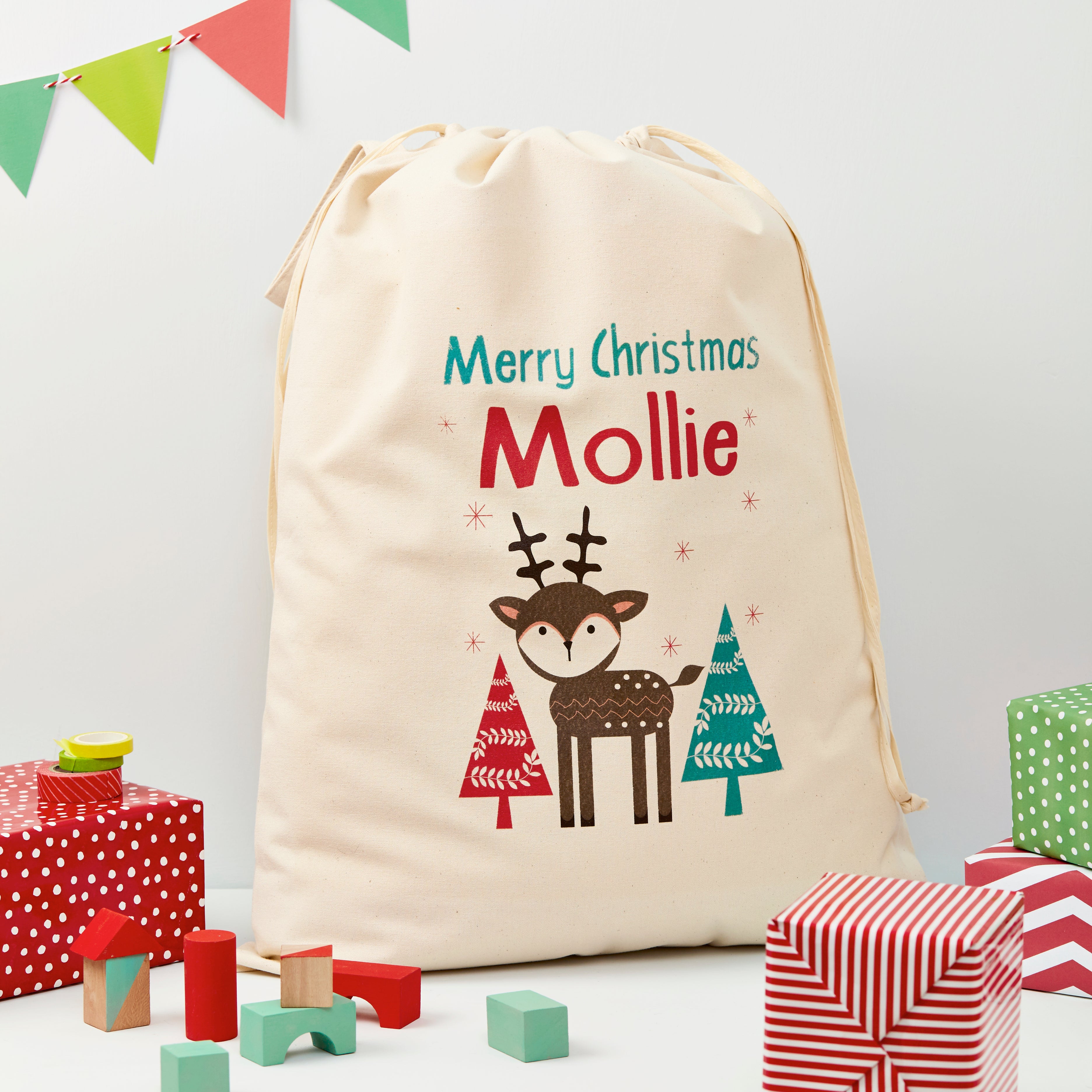 Personalized Christmas sack with reindeer design and text, surrounded by festive presents and decorations.