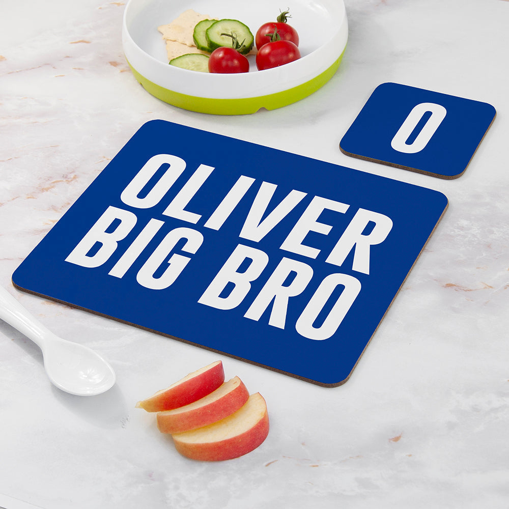 Blue placemat with 'OLIVER BIG BRO' text on a marble surface with fruit and a bowl.