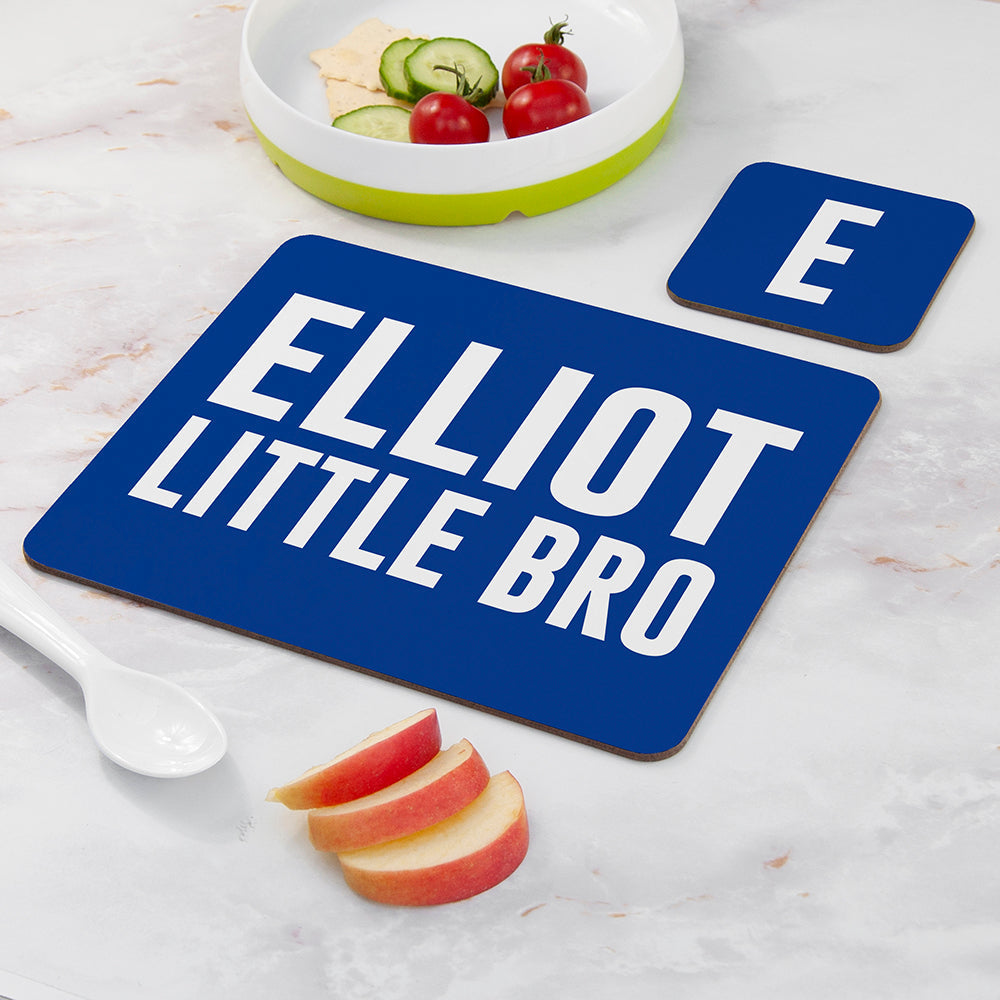 Blue placemat with 'ELLiot LITTLE BRO' text on a marble surface with fruit and a bowl.