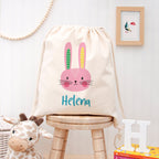 Drawstring bag with a rabbit design and 'Helena' text on a wooden stool, with a giraffe plush toy and books in the background.
