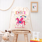 Drawstring bag with unicorn design and 'Holly' text on a wooden stool against a white wall.
