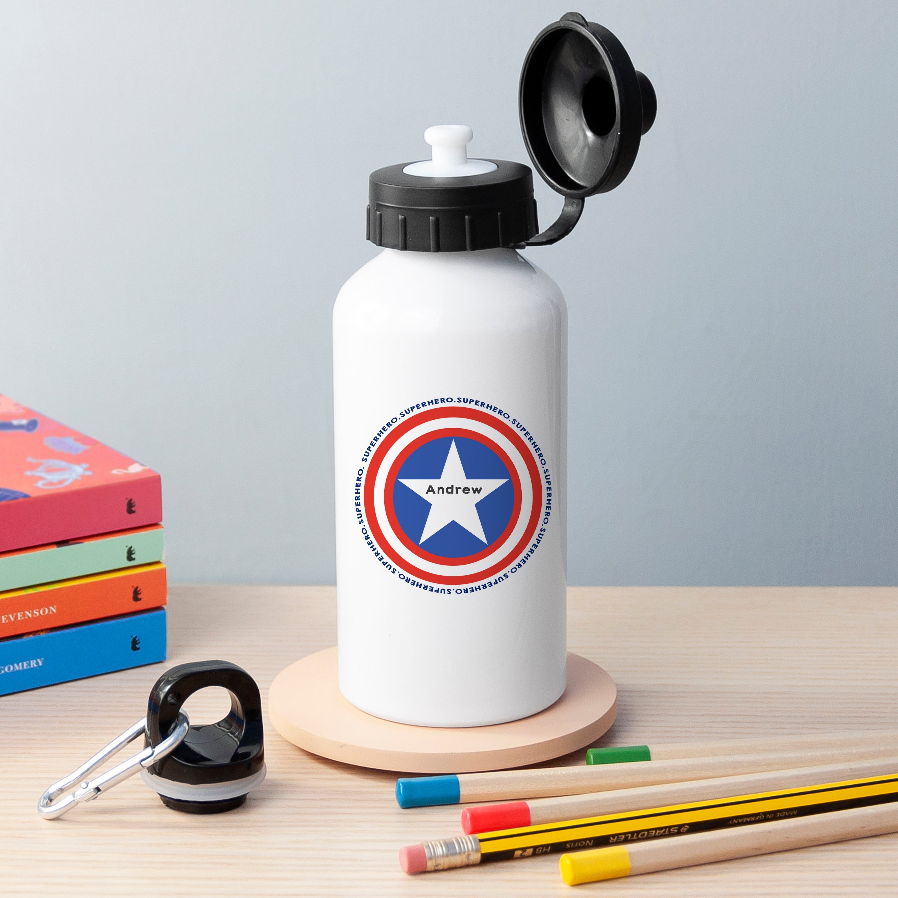 White water bottle with Captain America shield design on a wooden surface with books and pencils.