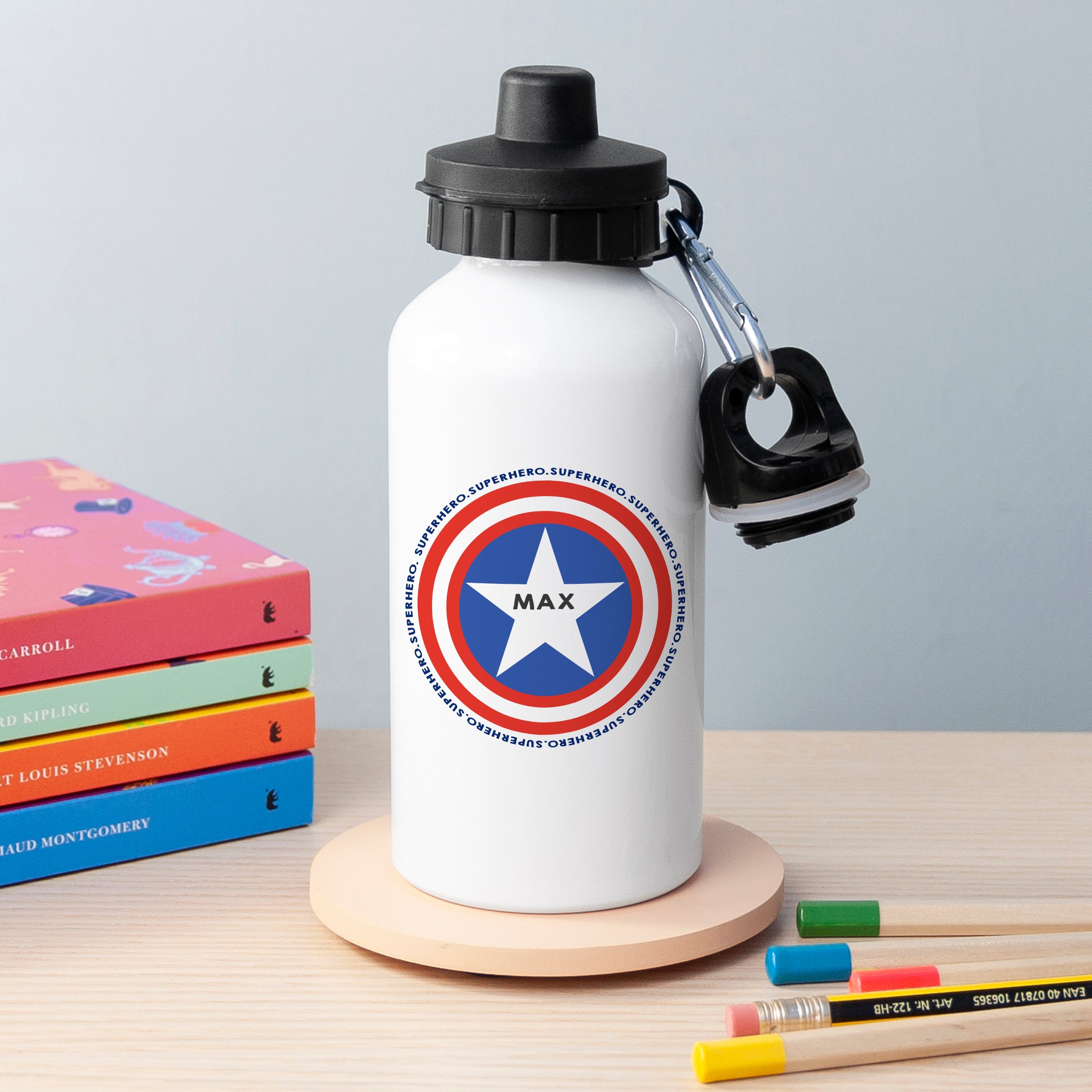 White water bottle with superhero emblem and 'MAX' text on a wooden surface with books and pencils.