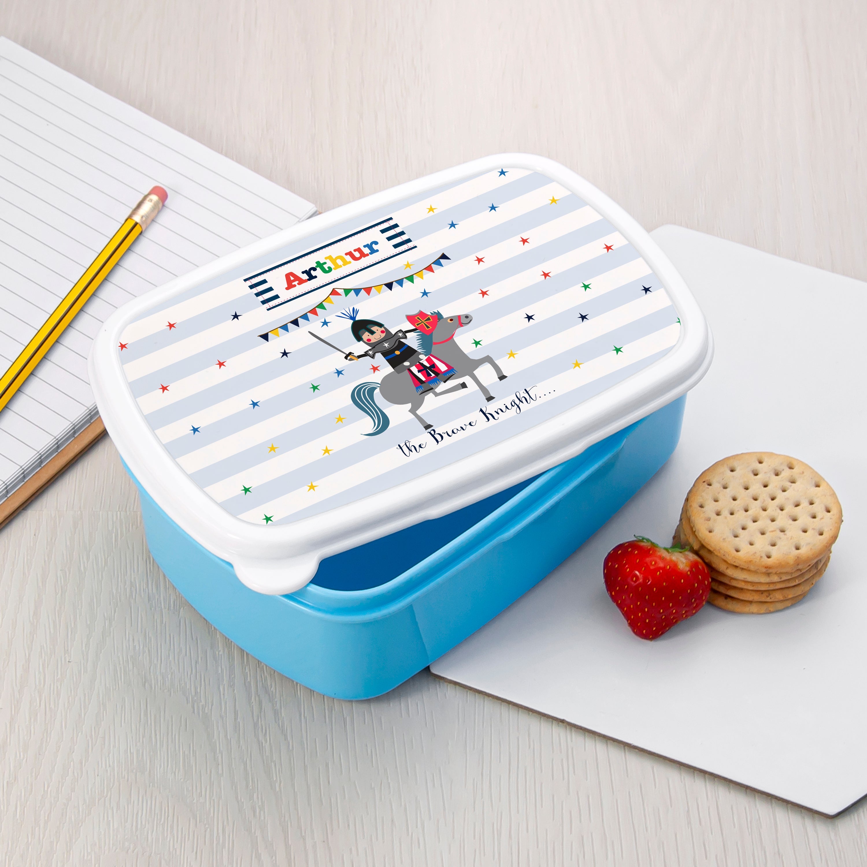 Blue lunch box with a colorful design on a white surface with a pencil and snacks.