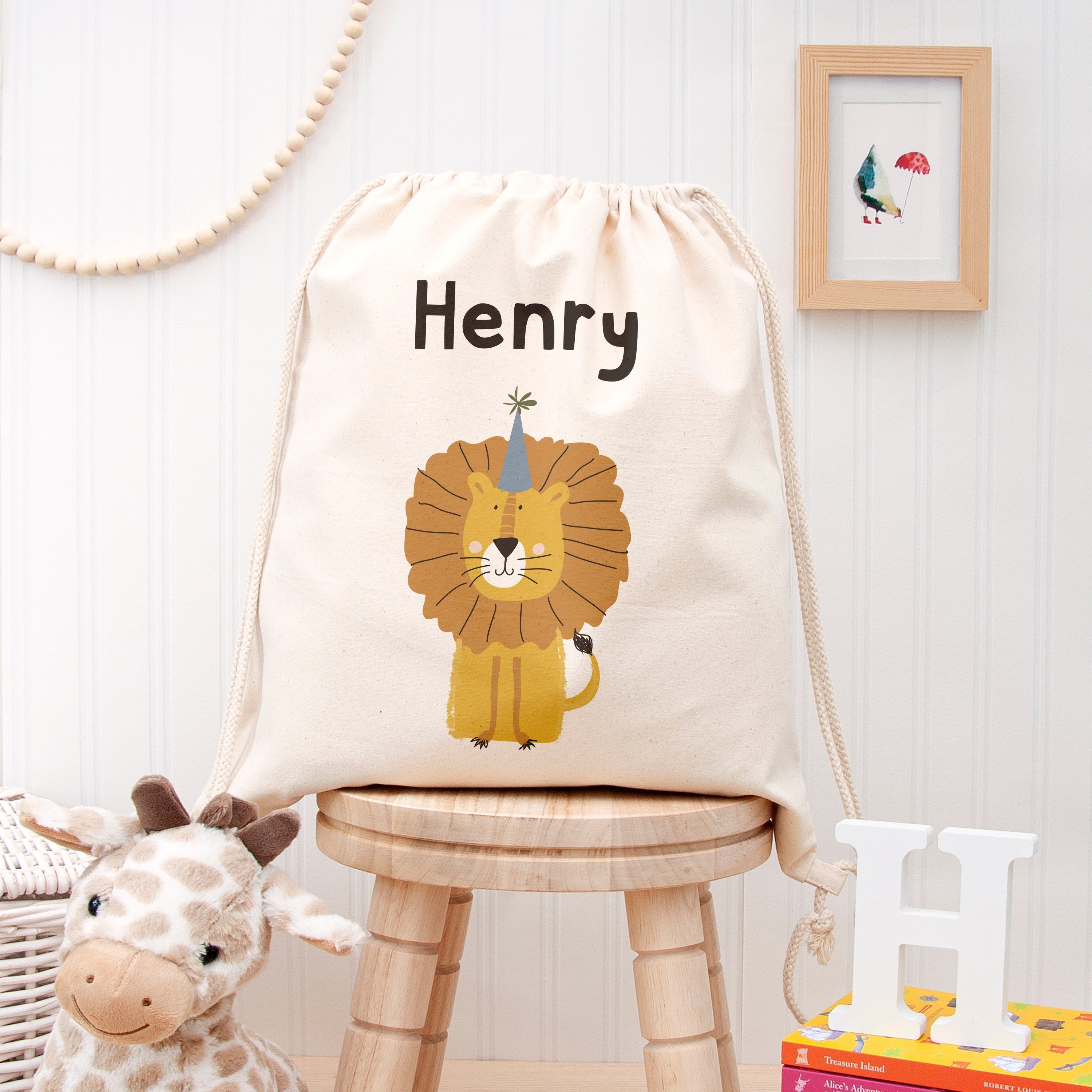 Drawstring bag with lion design and 'Henry' text on a wooden stool, with toys and books in the background.