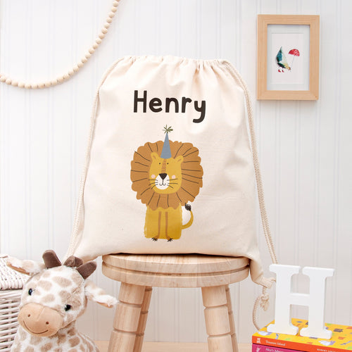 Drawstring bag with lion design and 'Henry' text on a wooden stool, with toys and books in the background.
