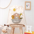 Drawstring bag with animal illustrations and 'Hazel' text on a wooden stool in a child's room.
