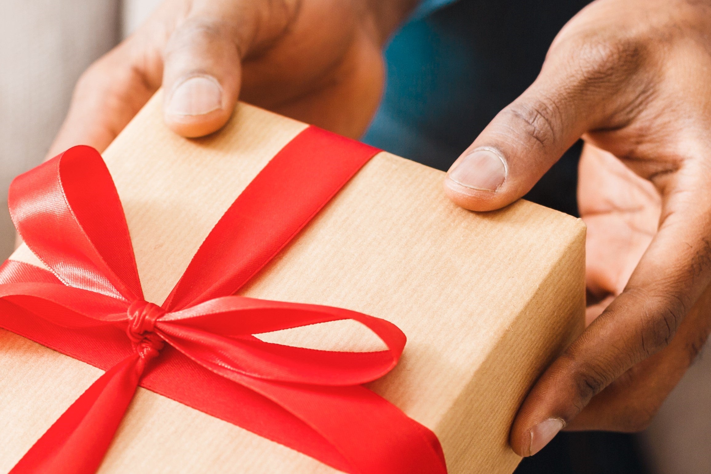 Hands holding a gift box with a red ribbon
