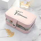 Pink jewelry box with 'Florence' branding on a marble surface with a necklace and leaf decoration.