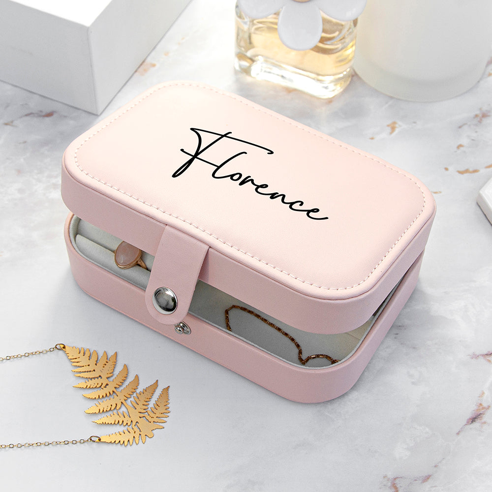 Pink jewelry box with 'Florence' branding on a marble surface with a necklace and leaf decoration.