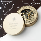 Gold compass with engraved text on a white surface