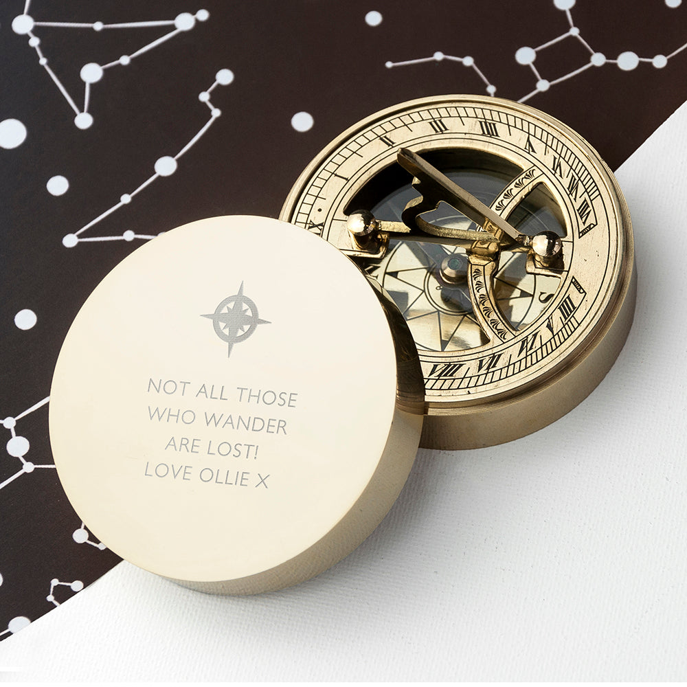 Gold compass with engraved text on a white surface