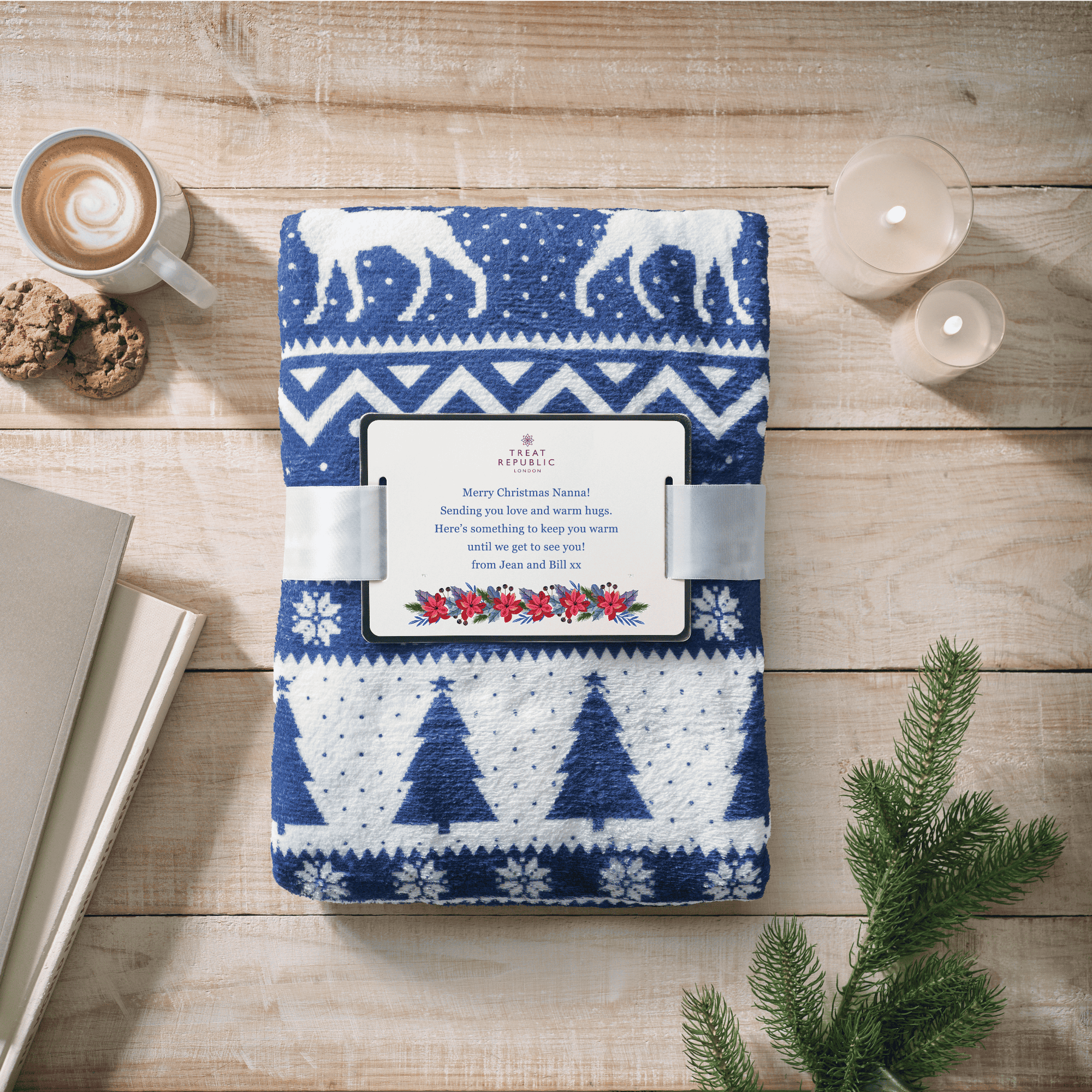 Blue and white patterned blanket with a Christmas design on a wooden surface with a cup of coffee and cookies.