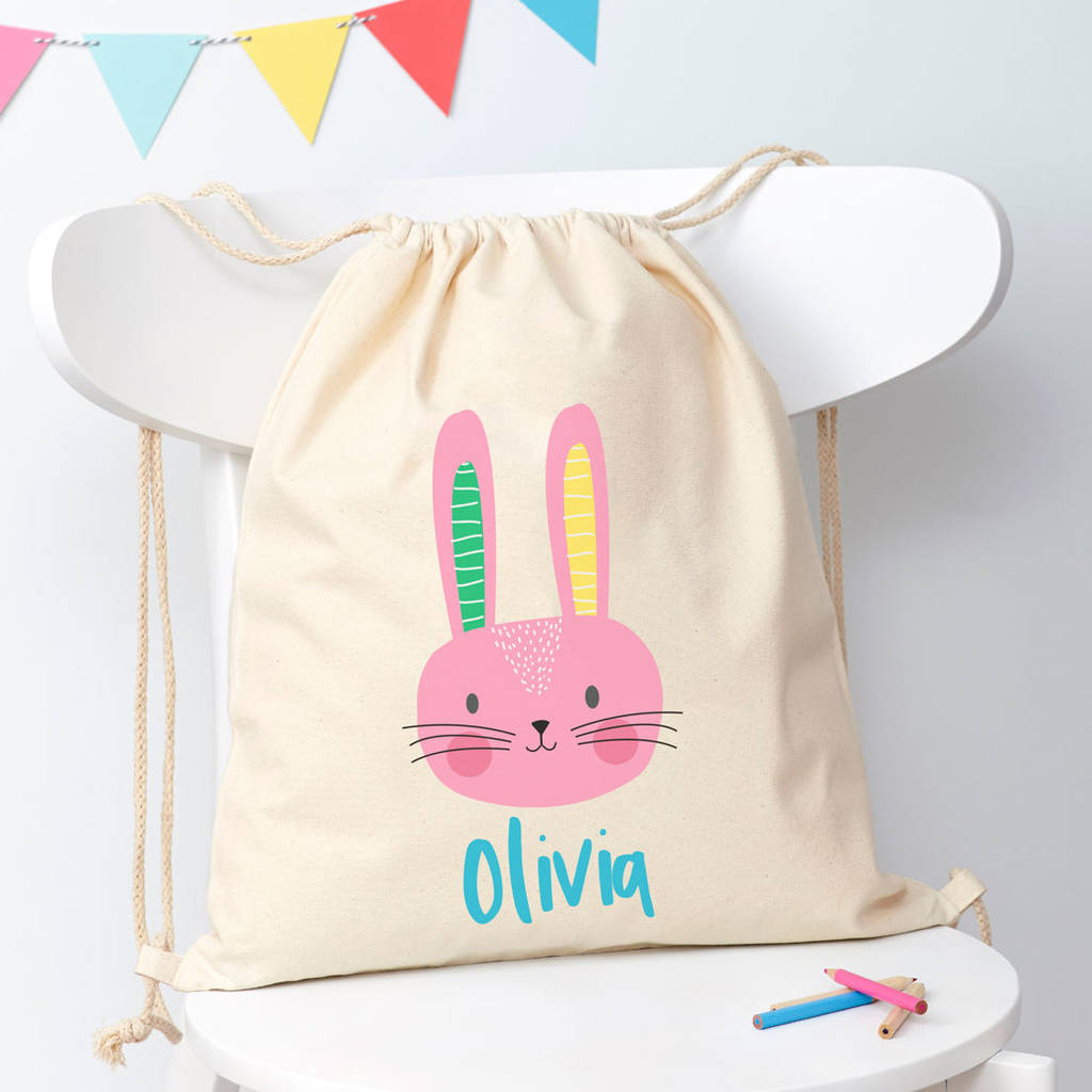 Canvas drawstring bag with a pink bunny design and 'Olivia' text on a white chair.