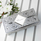 Decorative silver box with floral patterns on a white surface with a white flower in the background