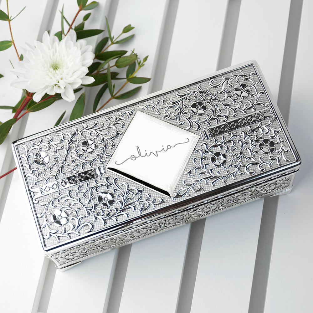 Decorative silver box with floral patterns on a white surface with a white flower in the background