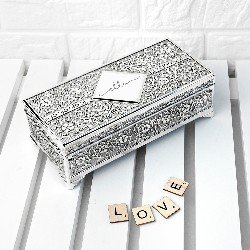 Decorative silver box with intricate patterns on a white surface with 'LOVE' spelled out with wooden letters.