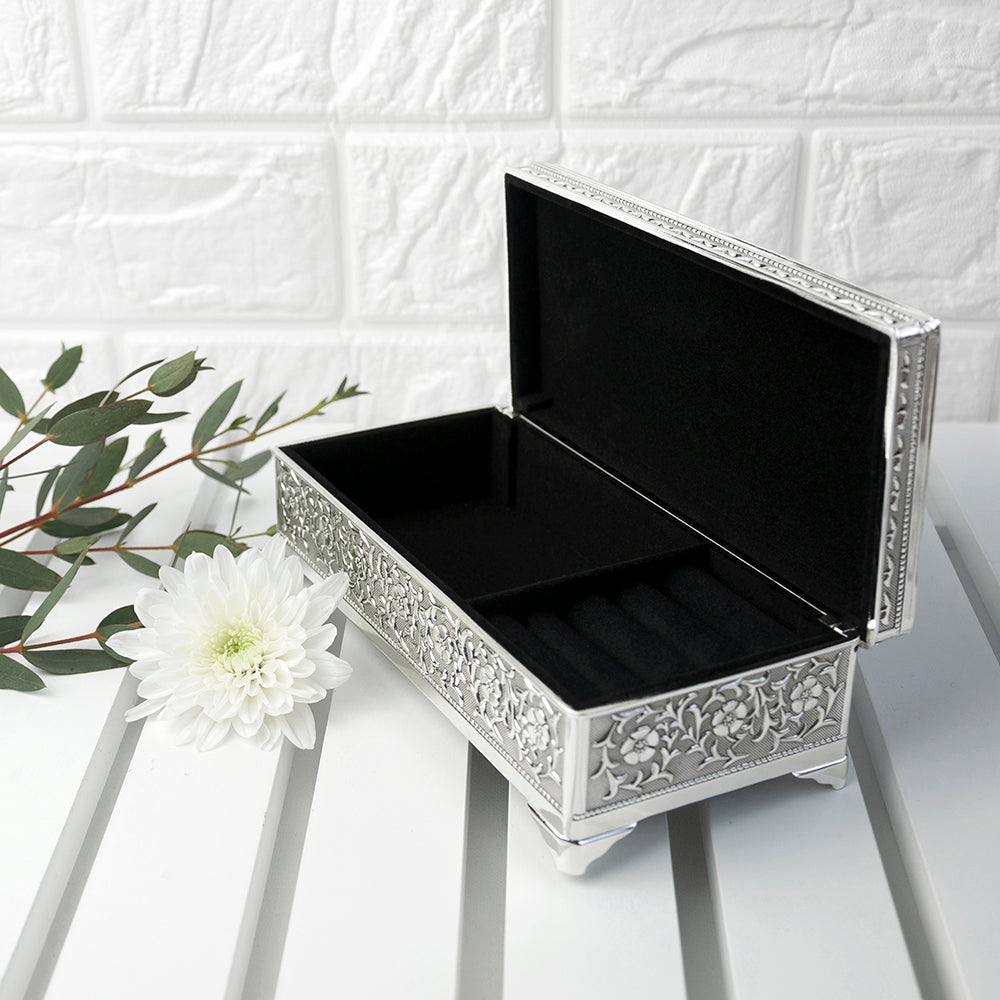 Decorative jewelry box with intricate patterns on a white surface with a white flower and green leaves.