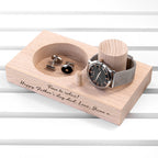 Wooden jewelry display with watch, cufflinks, and a message on a white background