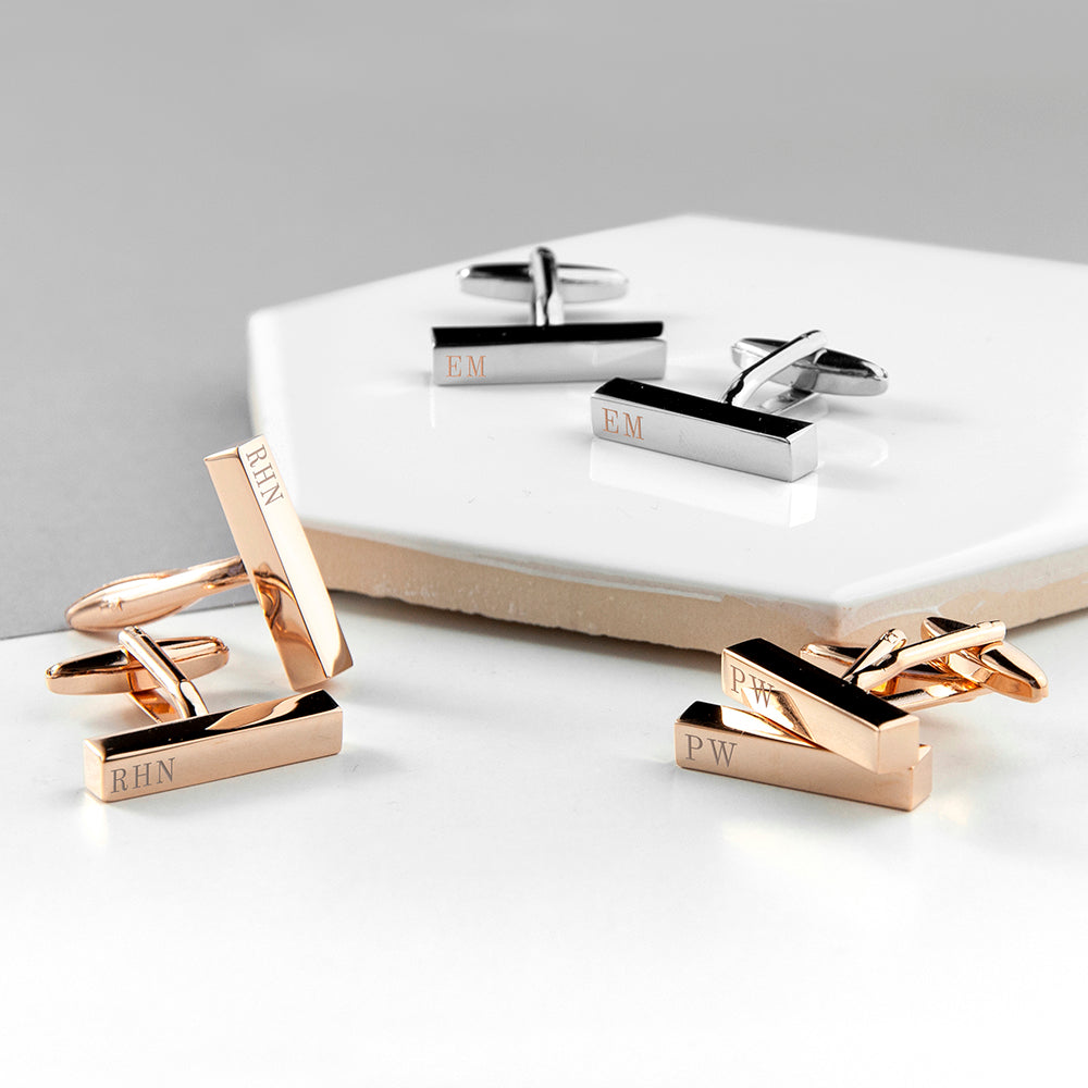 Gold and silver cufflinks with engraved initials on a white surface.