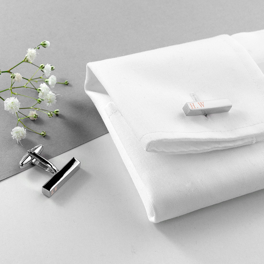 Cufflinks and a tie clip on a white shirt with flowers on a gray surface