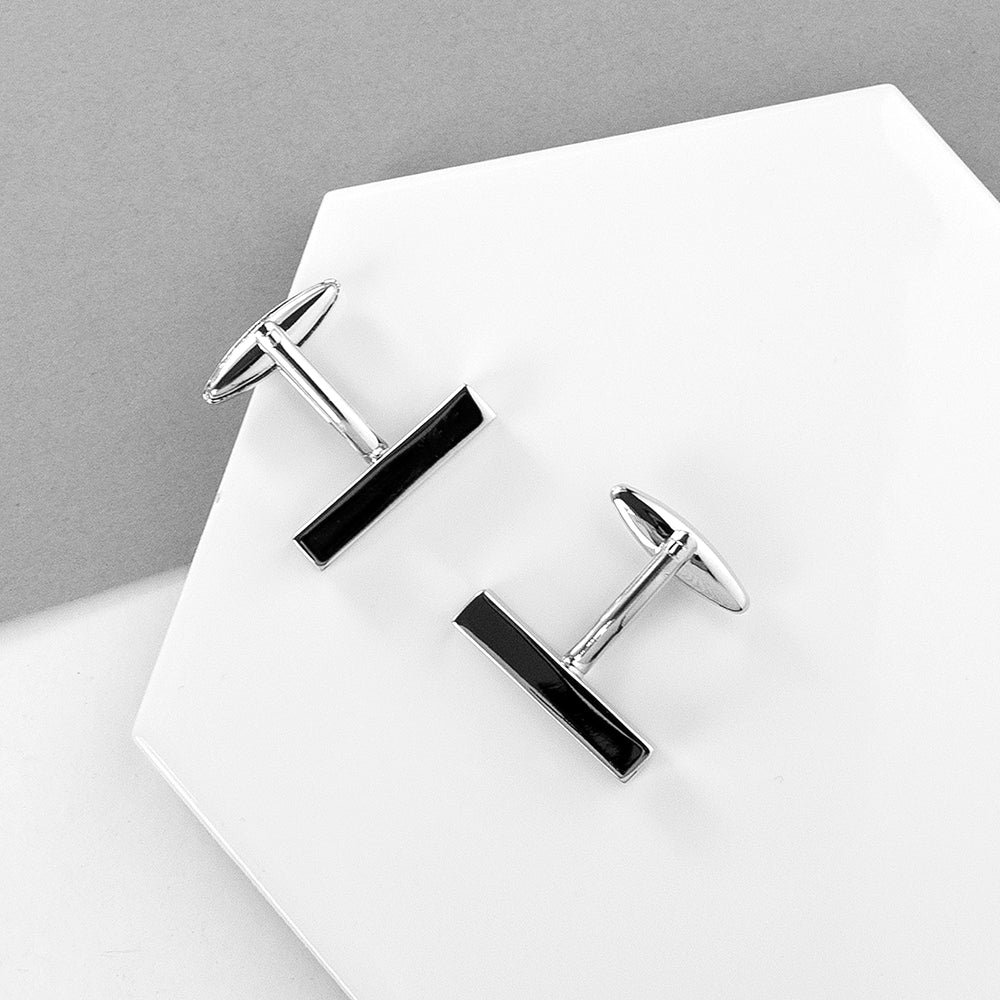 Pair of black and silver cufflinks on a white surface with a gray background