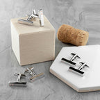 Silver cufflinks on a gray surface with a cork and wooden block.