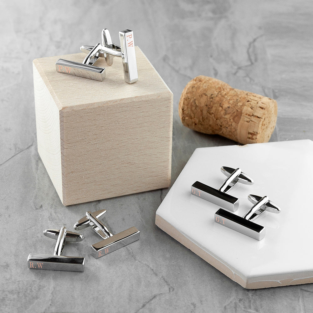 Silver cufflinks on a gray surface with a cork and wooden block.