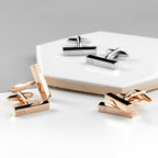 Gold and silver cufflinks with engraved initials on a white surface.